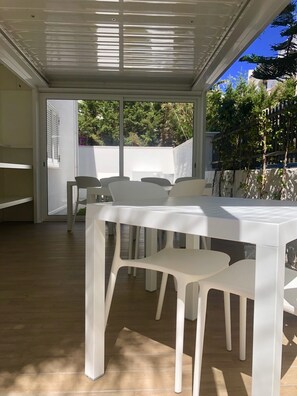 An outdoor patio area with a white table and chairs, a ceiling with horizontal slats, and a view of trees and a fence. - B&B Gassa D’Amante (Vieste)