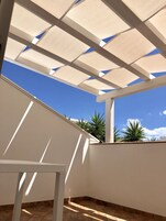 Un'area esterna riparata con struttura a soffitto bianca, un muro bianco e un pavimento piastrellato.