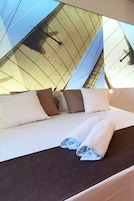 Un letto con cuscini bianchi e marroni, un asciugamano bianco ordinatamente piegato e vista dell'esterno dell'edificio attraverso una finestra.