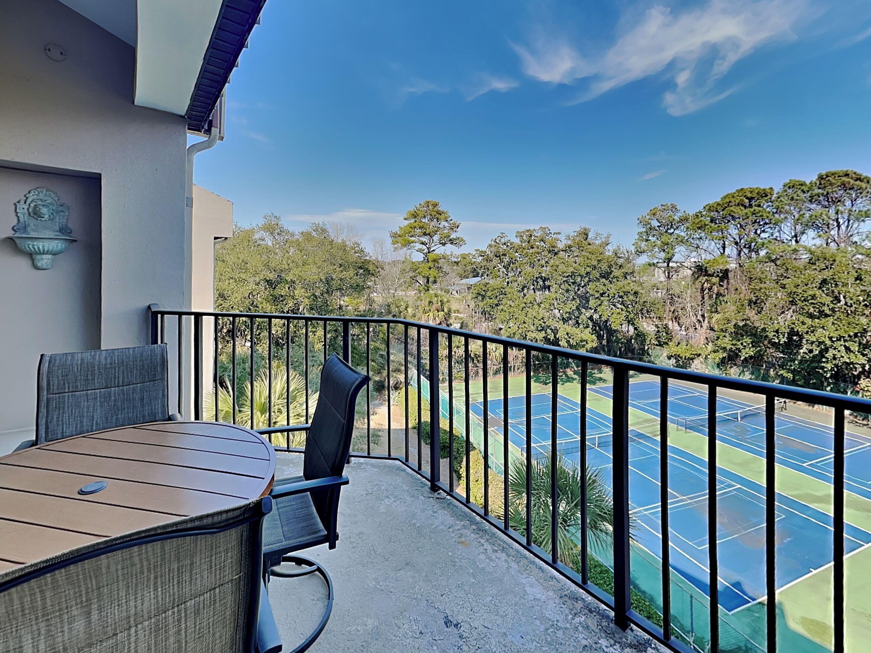 A balcony with a table and chairs, overlooking a tennis court.