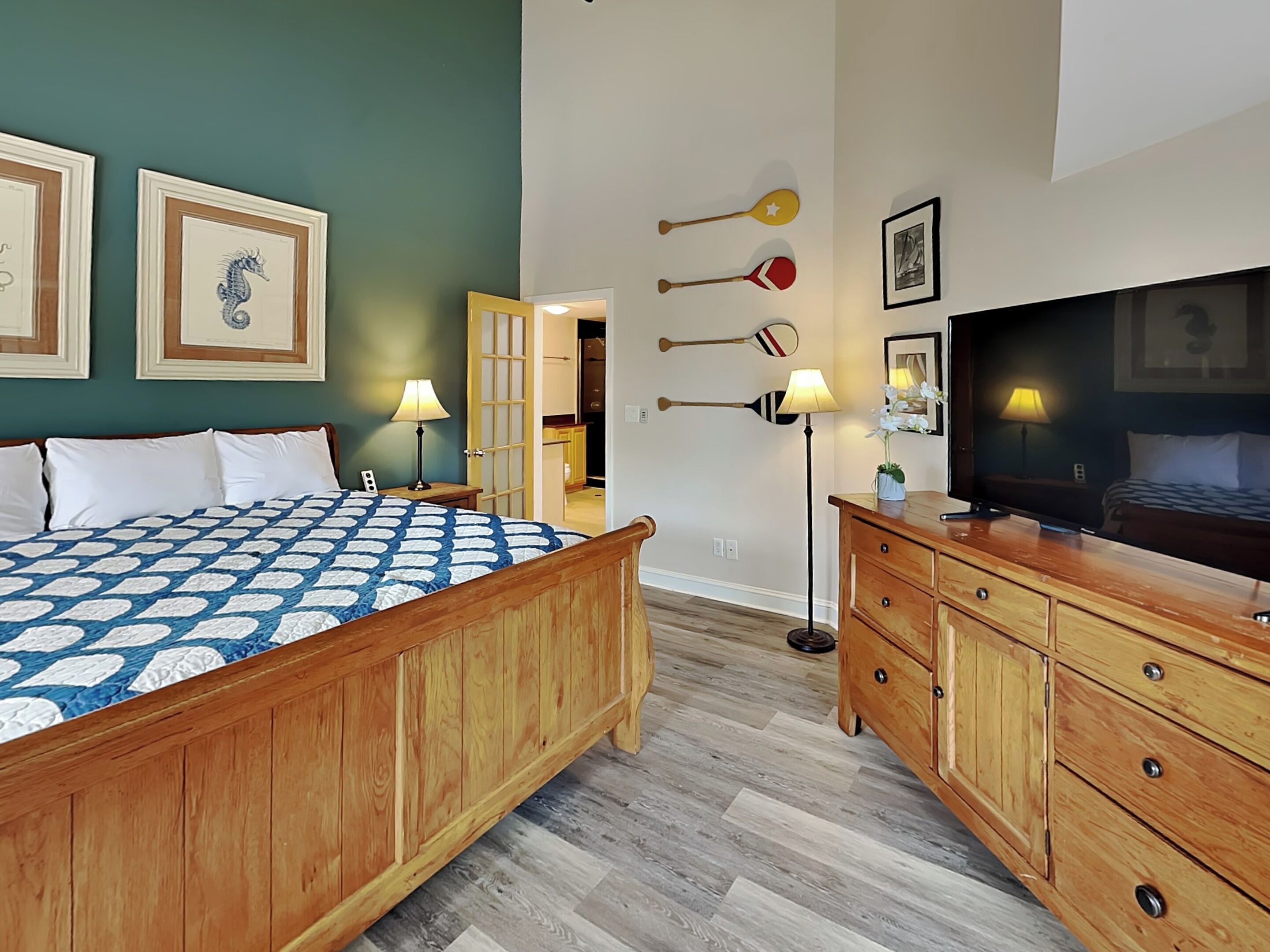 Un dormitorio con cama de madera, televisor, cómoda y equipo deportivo en la pared.