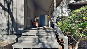 A wooden staircase leading to a porch with a blue door, a wicker chair, and a white railing. - Hickory Cove 47 by Hilton Head Retreats (Hilton Head Island)