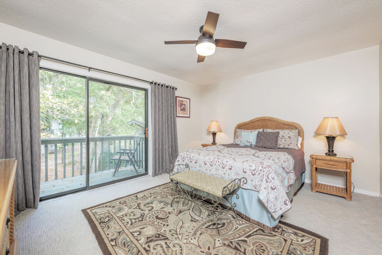 A bedroom with a large window, a ceiling fan, a bed with two bedside tables, and a chair.