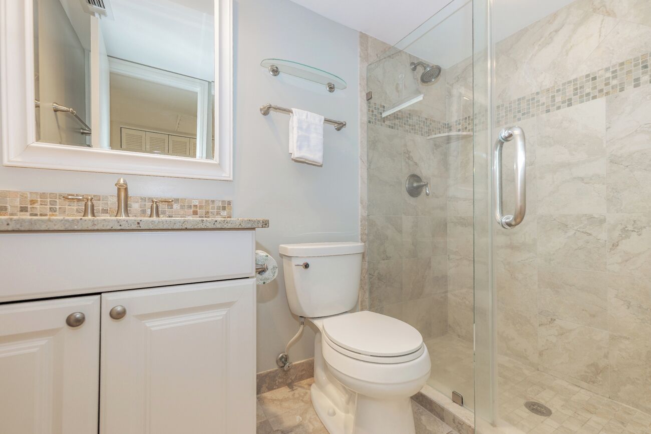 A modern bathroom with a glass-enclosed shower, a white toilet, and a tiled backsplash.