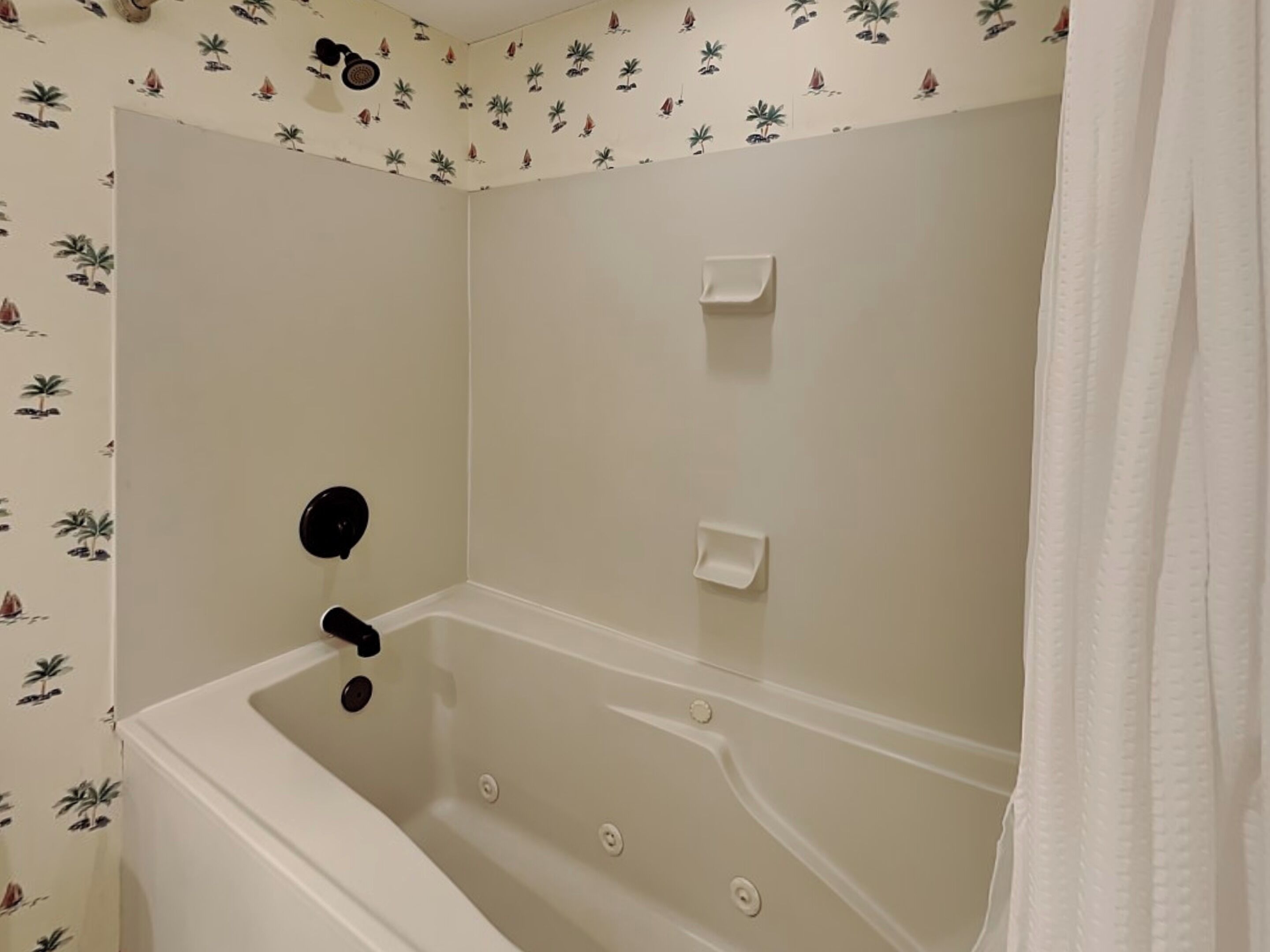 Un baño con bañera, cortina de ducha y un muro con estampado tropical.