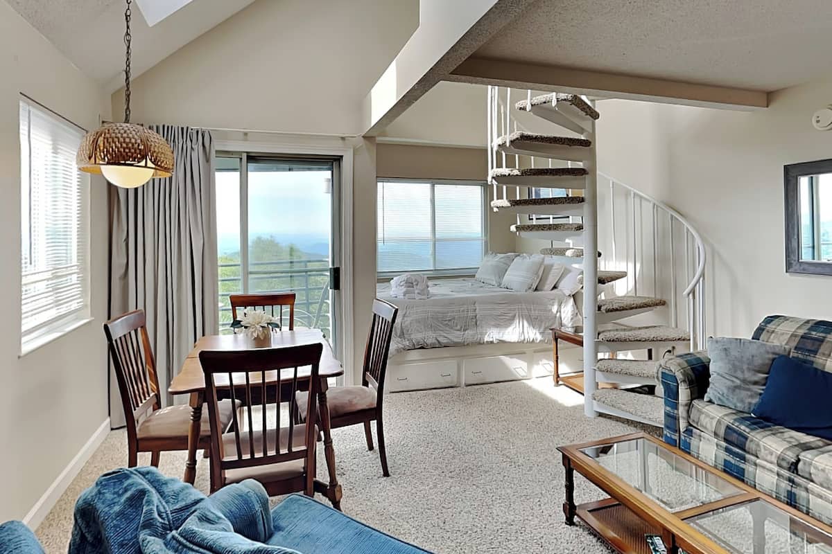 A spacious living area with a dining table, chairs, a sofa, a staircase, and a view of the outdoors.