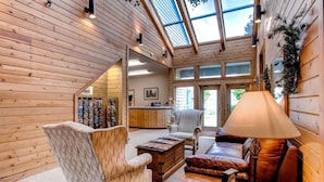 A spacious room with wooden walls, a high ceiling, and a skylight. There is a sofa, a chair, and a coffee table. - Summit of Gatlinburg by Jackson Mountain Rentals (Gatlinburg)