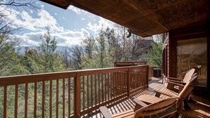 Eine Holzterrasse mit Adirondack-Stühlen und Blick auf einen bewaldeten Gebirgszug.