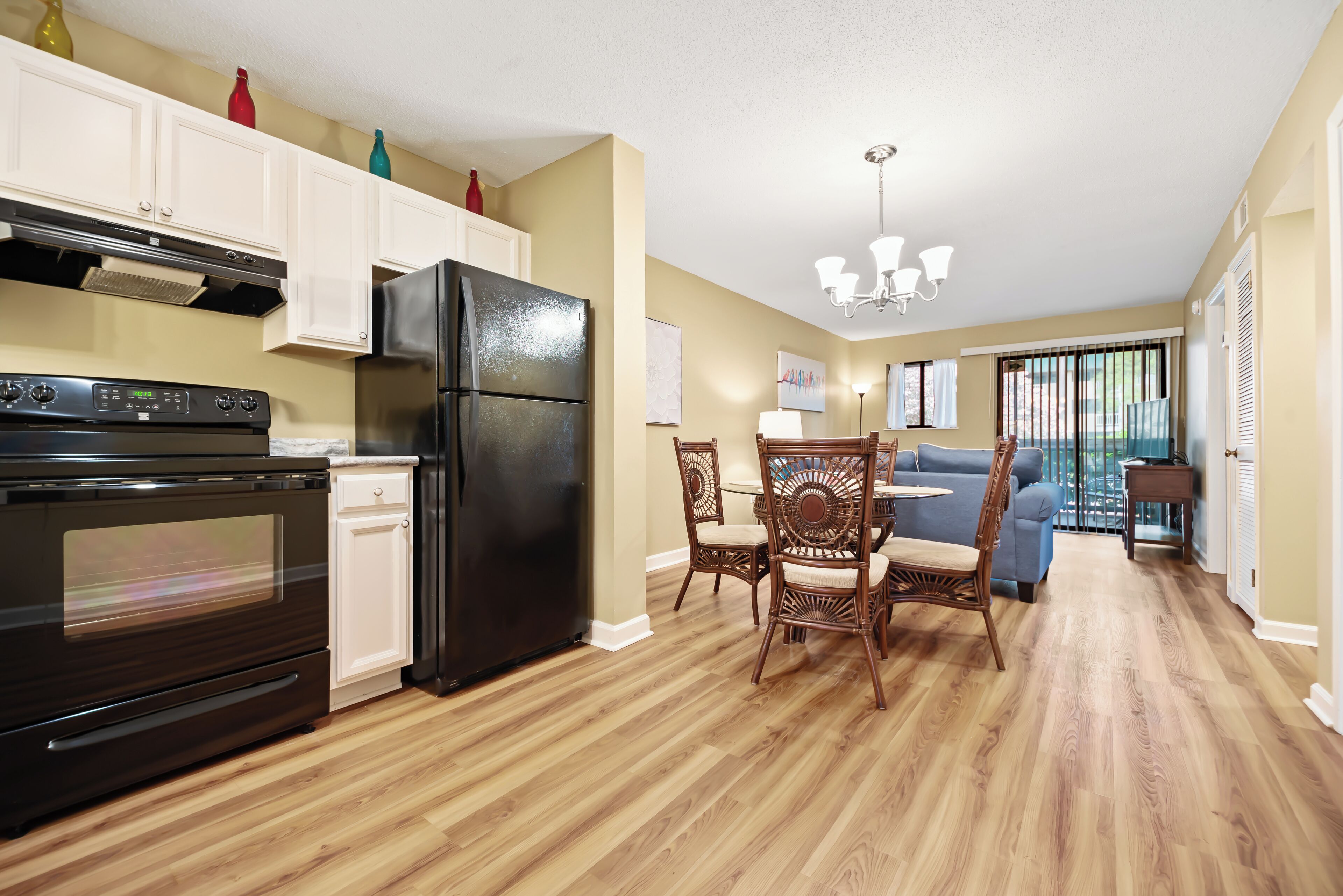 Una cocina con armarios blancos, un refrigerador negro y una mesa de comedor de madera con sillas.