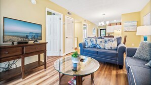 A living room with a television, a glass coffee table, a sofa, and a blue armchair. - The Spa by Hilton Head Retreats (Hilton Head Island)