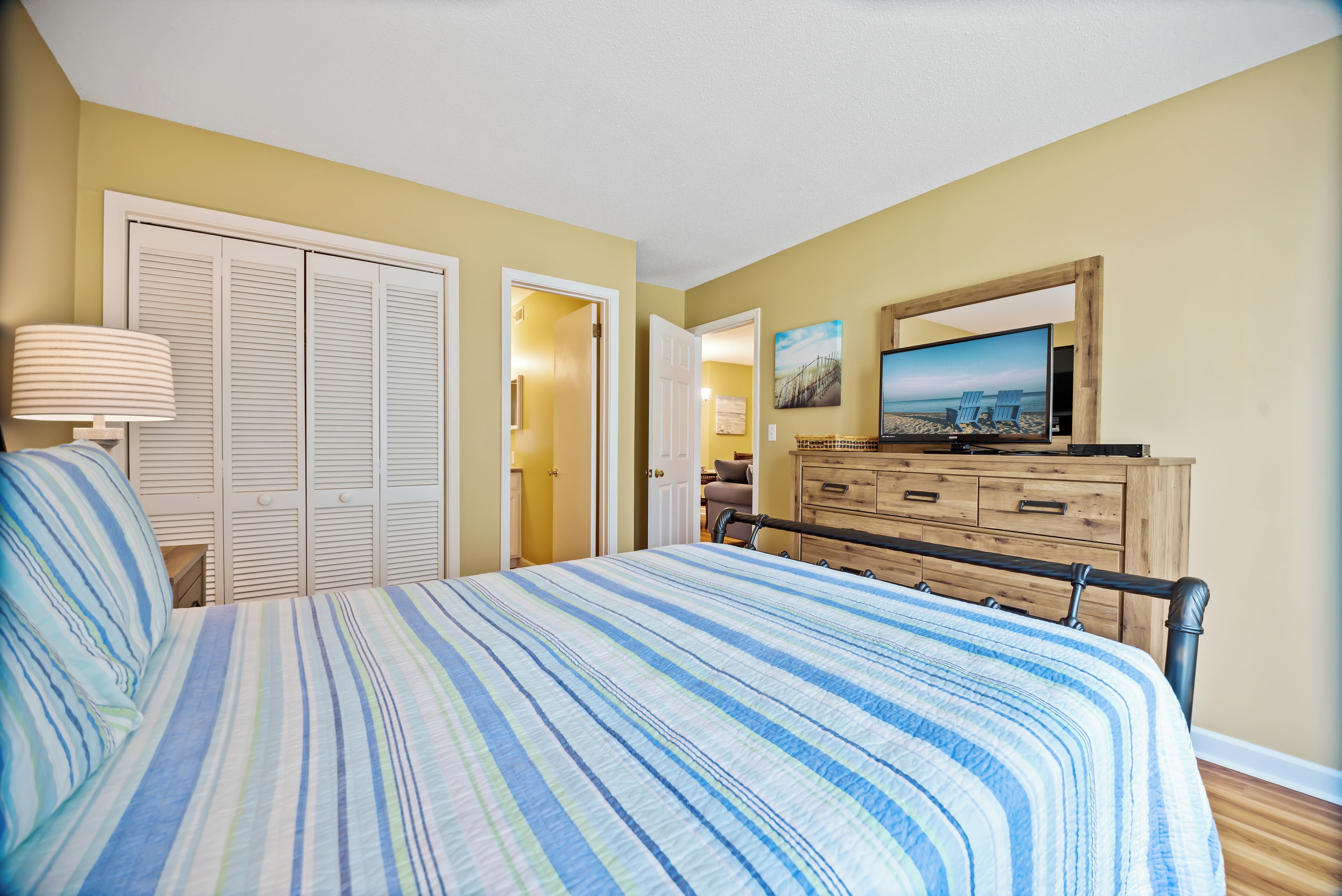 A bedroom with a bed, a dresser, a television, and a door leading to another room.