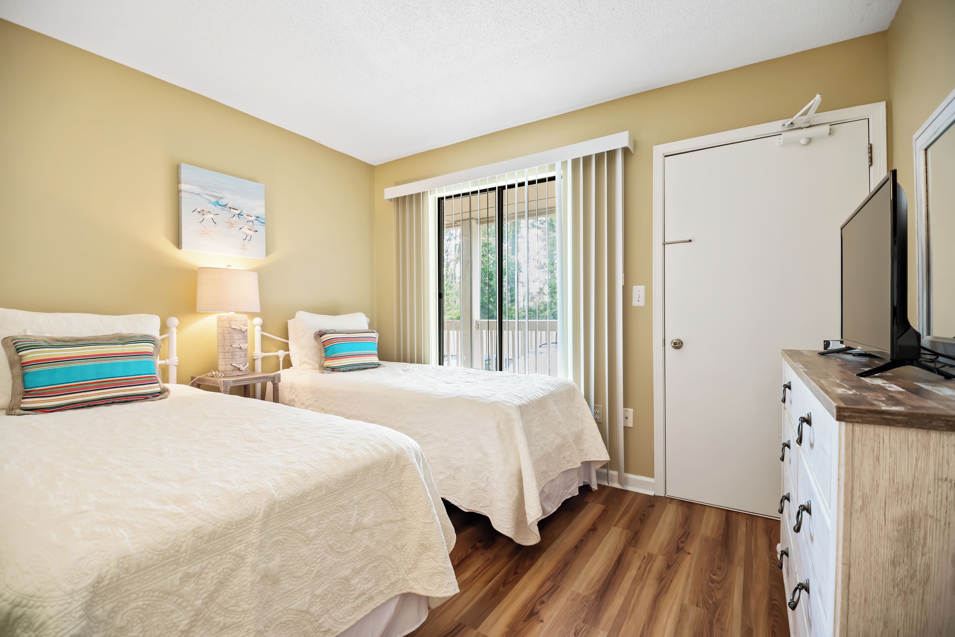 A hotel room with two beds, a wooden dresser, a TV, and a window with curtains.