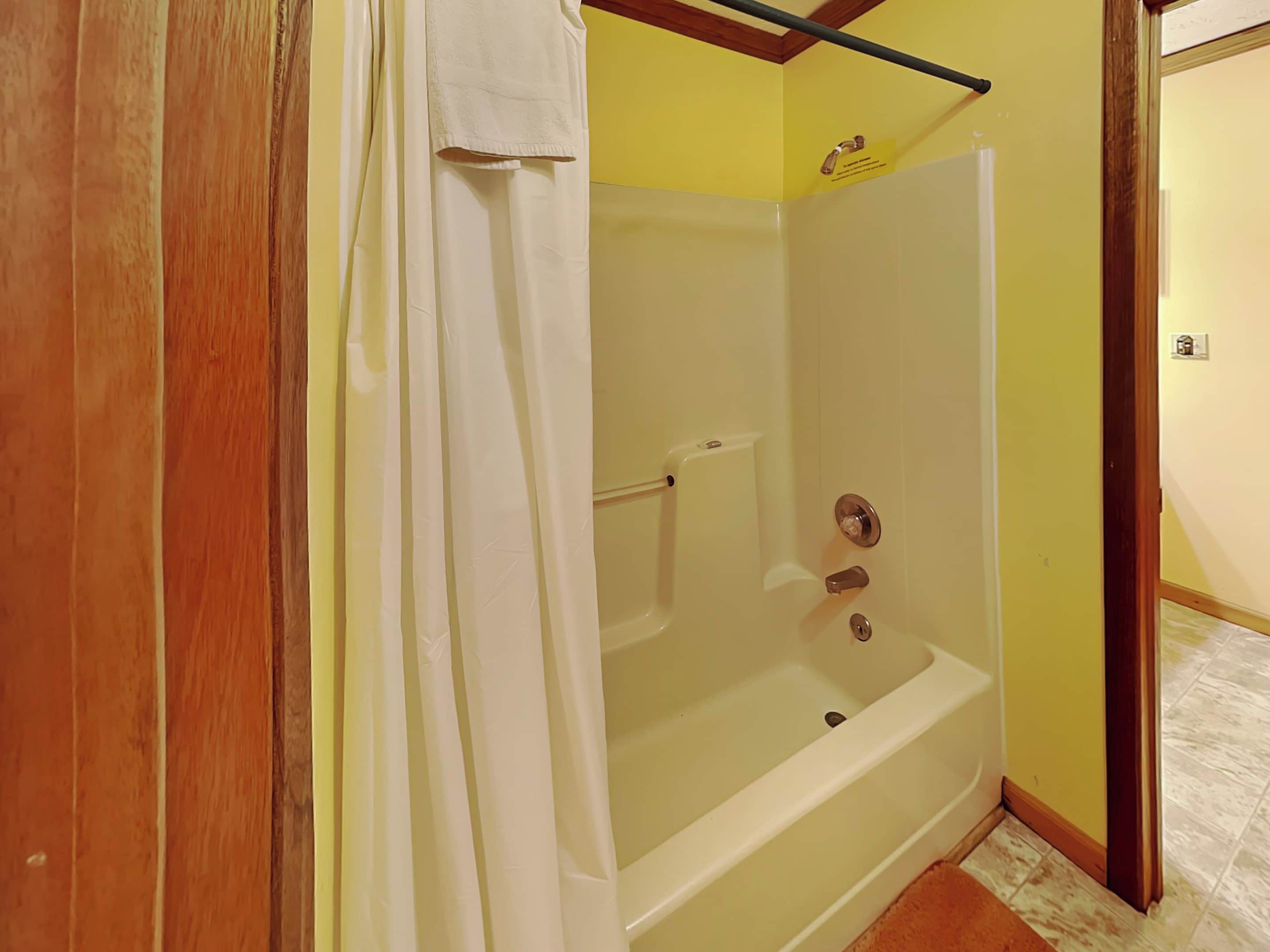 Ducha con cortina blanca, un perchero y un letrero que indica un sistema de ahorro de agua.