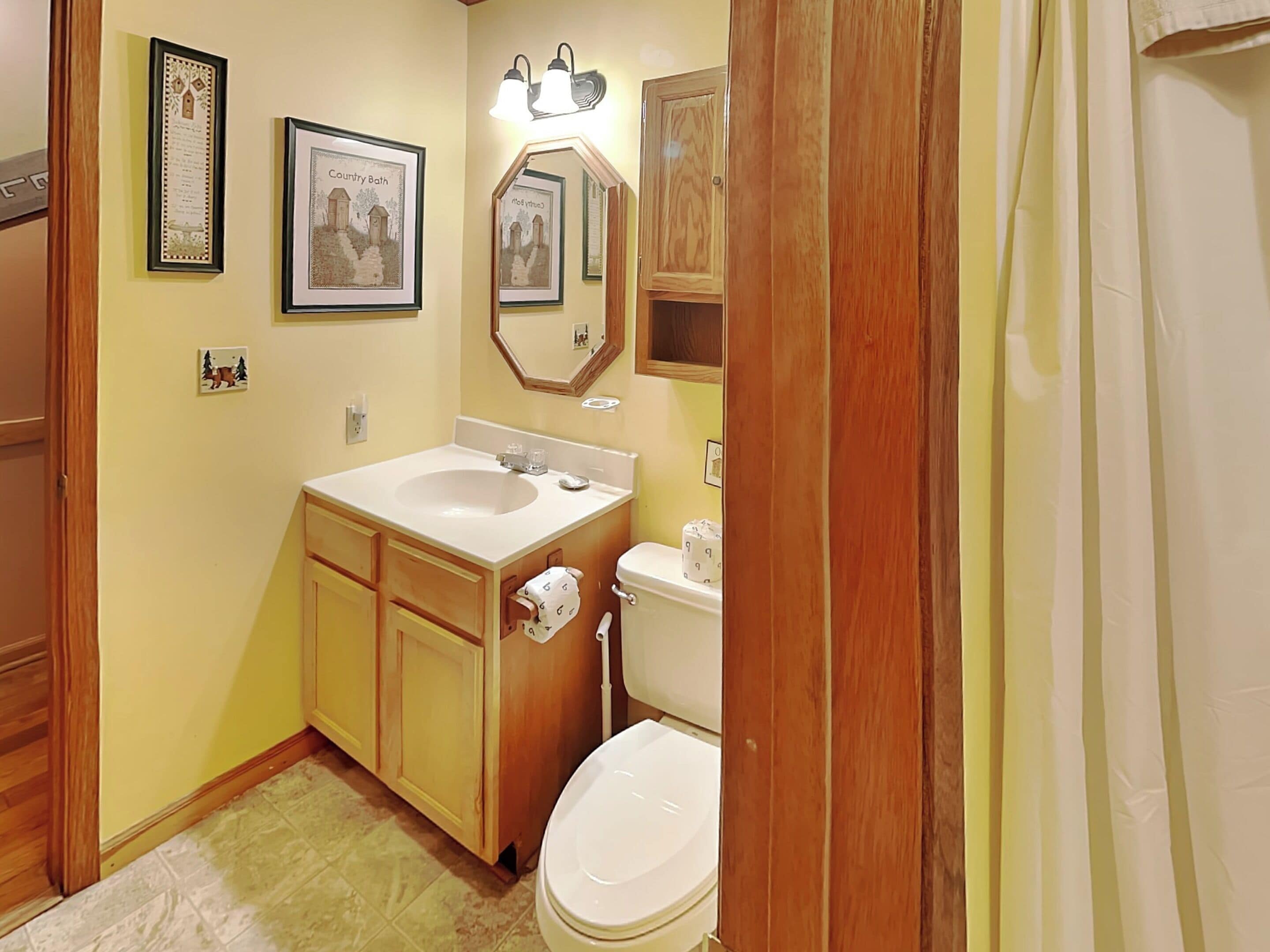 A bathroom with a wooden vanity, a sink, a toilet, and framed pictures on the wall.