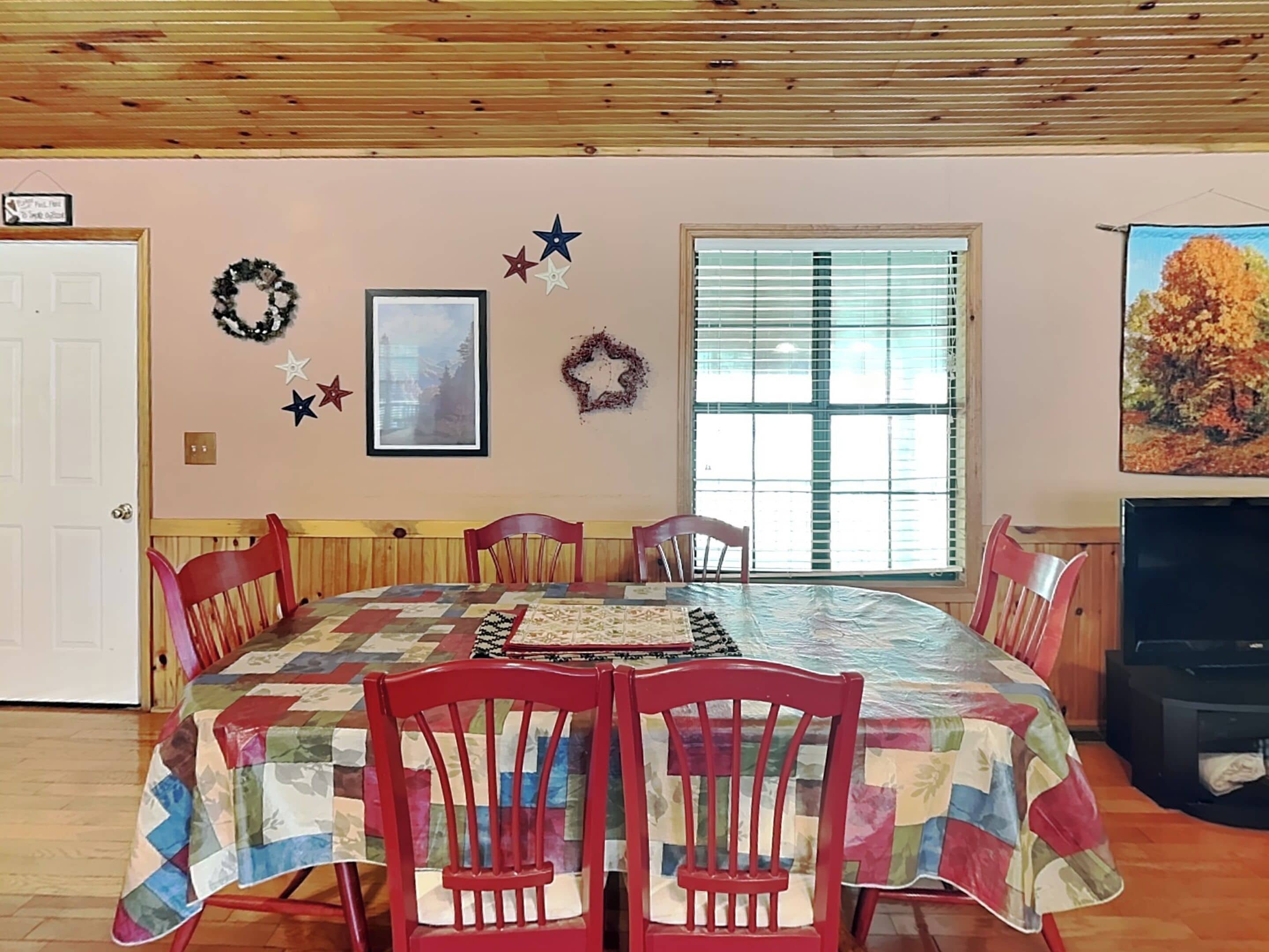 Un comedor con una mesa y sillas de madera, una ventana con persianas, y adornos en la pared como estrellas y una guirnalda.