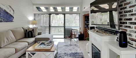 Una sala de estar moderna con sofá, mesa de centro, chimenea y ventanas amplias.