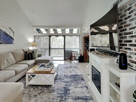 Una sala de estar moderna con sofá, mesa de centro, chimenea y ventanas amplias.