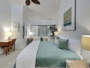 Ein Schlafzimmer mit einem großen Bett, zwei Nachttischen mit Lampen, einem Schreibtisch mit Stuhl und einem Fenster mit Jalousien.