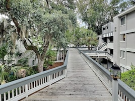 Un puente de madera que conecta dos edificios con balcones, rodeado de árboles y follaje.