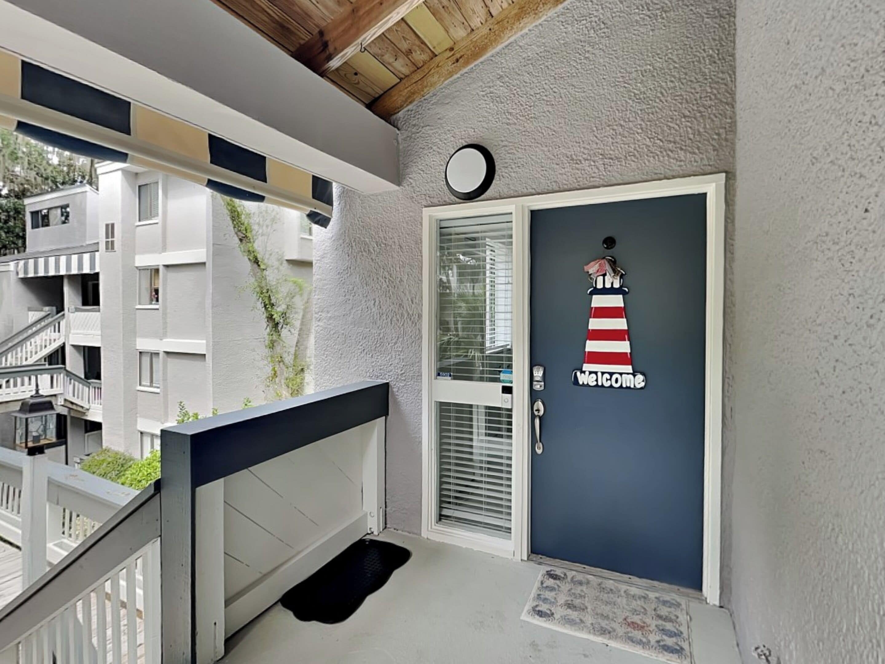 Een gebouwentree met een 'Welcome'-bord, een deur met strepen en een zwarte mat bij de ingang.