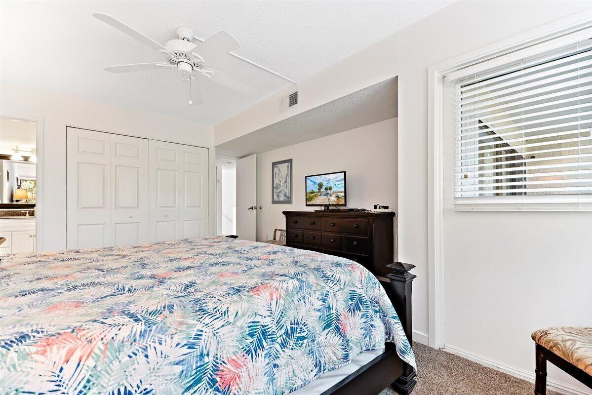A bedroom with a bed, a ceiling fan, a dresser, a window with blinds, and a door.