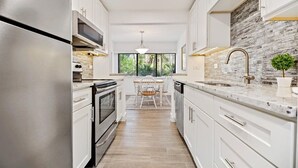 Une cuisine moderne avec des meubles blancs, des appareils en acier inoxydable et un pare-feu en pierre.