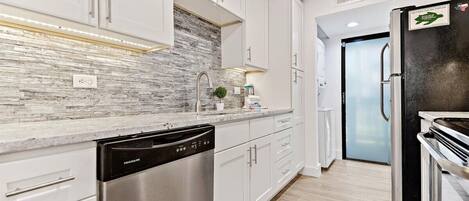 A modern kitchen with white cabinets, a stainless steel dishwasher, a black refrigerator, and a tiled backsplash.