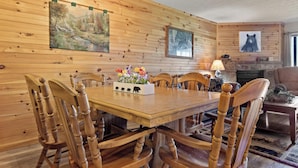 A wooden-paneled dining room with a table and chairs, a fireplace, and wall-mounted artwork. - Bear Cub Retreat by Jackson Mountain Rentals (Gatlinburg)