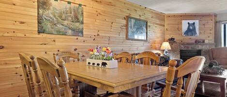 Uma sala de jantar com painéis de madeira, uma mesa, cadeiras, lareira e obras de arte penduradas na parede.