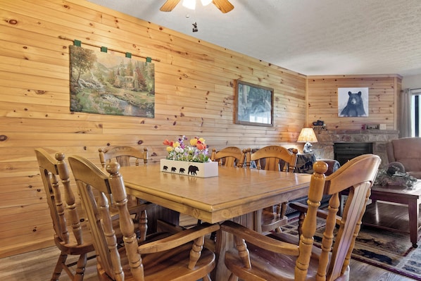 Een eetkamer met houten lambrisering, een tafel en stoelen, een open haard en kunstwerken aan de muur.