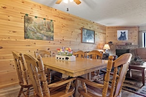 A wooden-paneled dining room with a table and chairs, a fireplace, and wall-mounted artwork.
