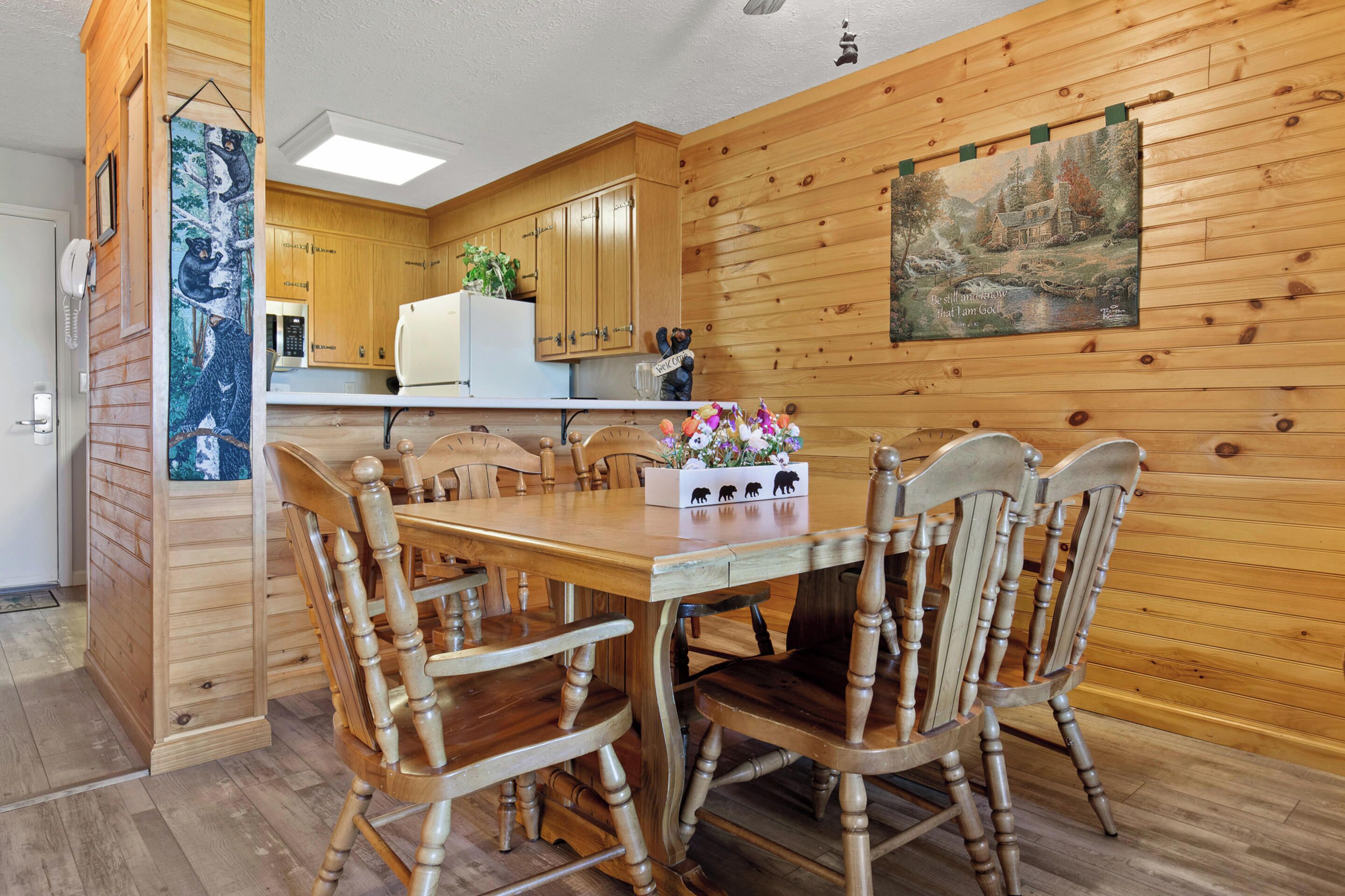 A wooden-paneled room with a dining table and chairs, a kitchen area with wooden cabinets, and a painting on the wall.
