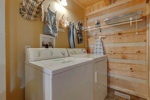 Un área de lavandería con lavadora y secadora de carga frontal, paredes de madera y un tendedero con ropa.