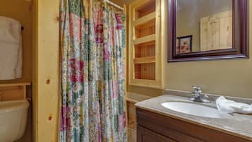 A bathroom with a wooden vanity, a sink, a mirror, and a shower curtain with floral patterns.