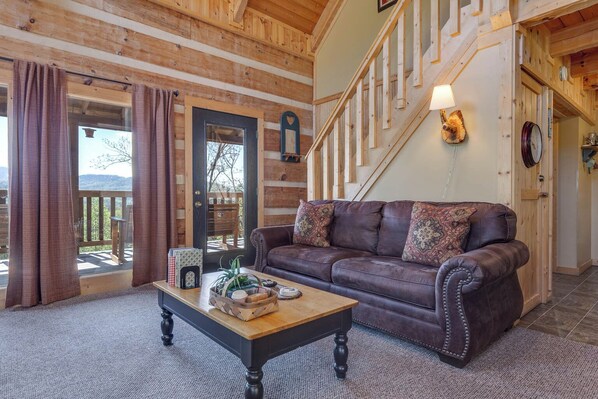 A cozy living room with a leather sofa, a wooden coffee table, and a staircase leading to an upper level. - Sweet Surrender by Jackson Mountain Rentals (Gatlinburg)