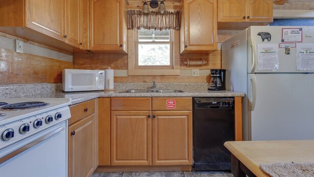 A compact kitchen with wooden cabinets, a microwave, a stove, a sink, and a refrigerator.