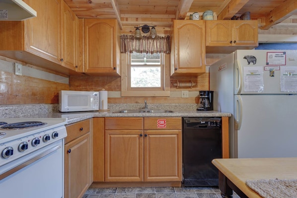 A compact kitchen with wooden cabinets, a microwave, a stove, a sink, and a refrigerator. - Sweet Surrender by Jackson Mountain Rentals (Gatlinburg)