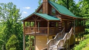 A wooden cabin with a green roof, a balcony, and a staircase leading to the upper level.