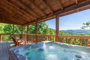 Una terraza de madera con jacuzzi y asientos, con vistas a un paisaje montañoso.