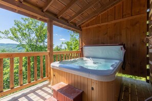 A wooden deck with a hot tub, wooden railings, and a view of a forested landscape. - Sweet Surrender by Jackson Mountain Rentals (Gatlinburg)