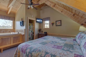 A bedroom with a wooden ceiling, a bed with a colorful quilt, a wooden dresser, a television, and a window with a view of trees. - Sweet Surrender by Jackson Mountain Rentals (Gatlinburg)