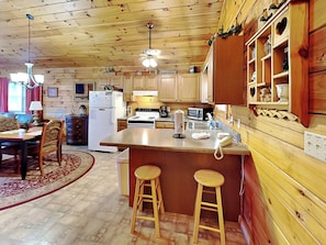 A cozy cabin-style kitchen with wooden cabinets, a central island with stools, a refrigerator, stove, and a microwave.