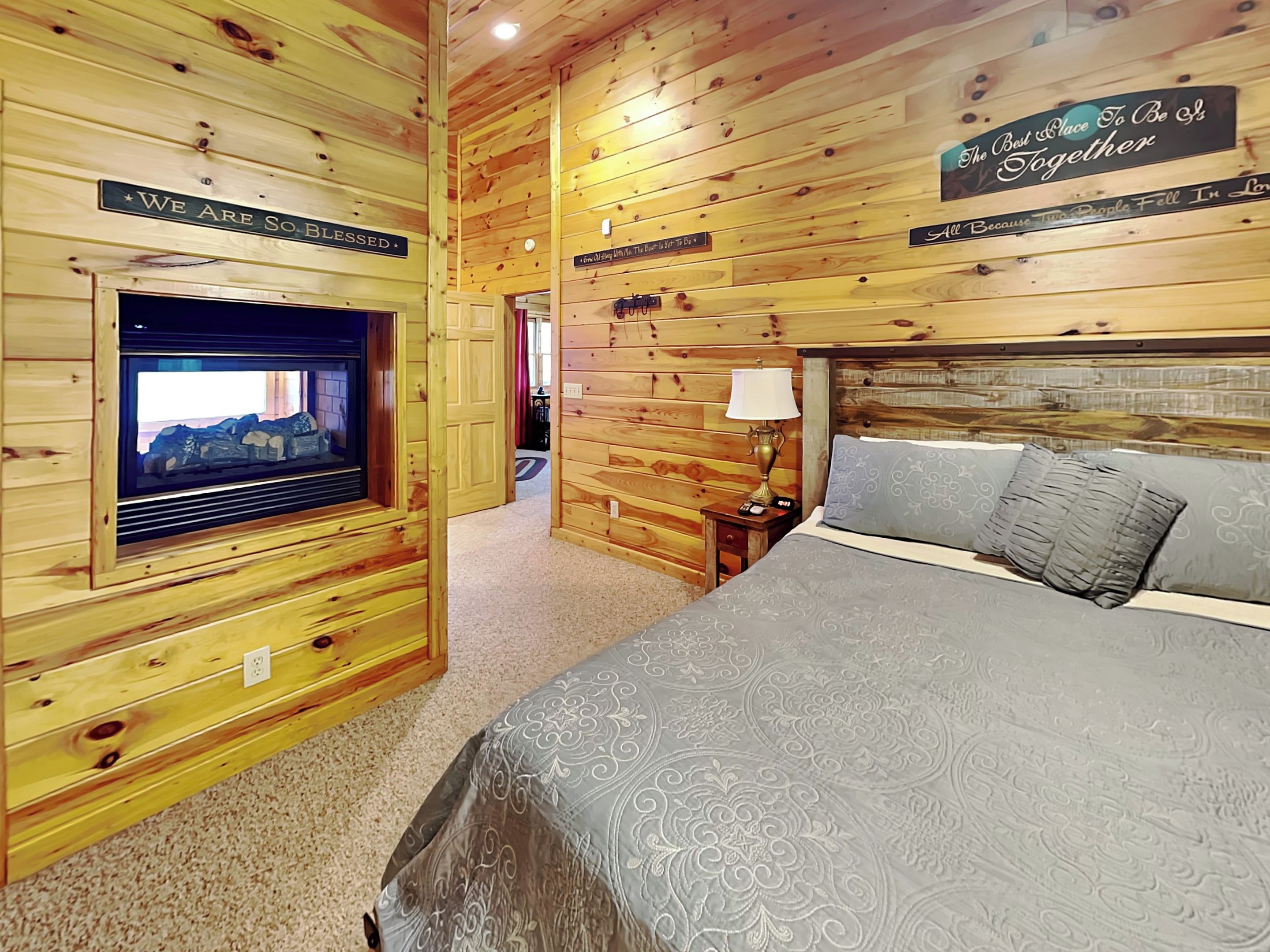 Una habitación acogedora con paredes de madera, una cama con ropa de cama estampada, un televisor y carteles con mensajes inspiradores.