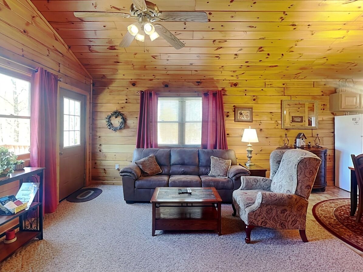A wooden interior with a sofa, armchair, coffee table, and a ceiling fan.