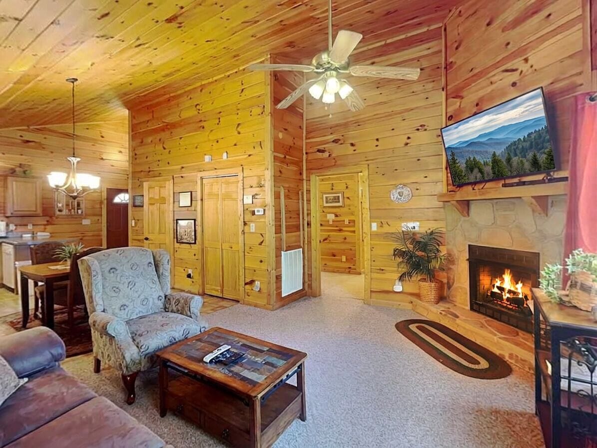A log cabin interior with a fireplace, a television, and a ceiling fan.