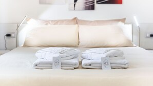 A neatly made bed with two pillows and two folded towels on a white bedspread. - Nùe Rooms (Cagliari)