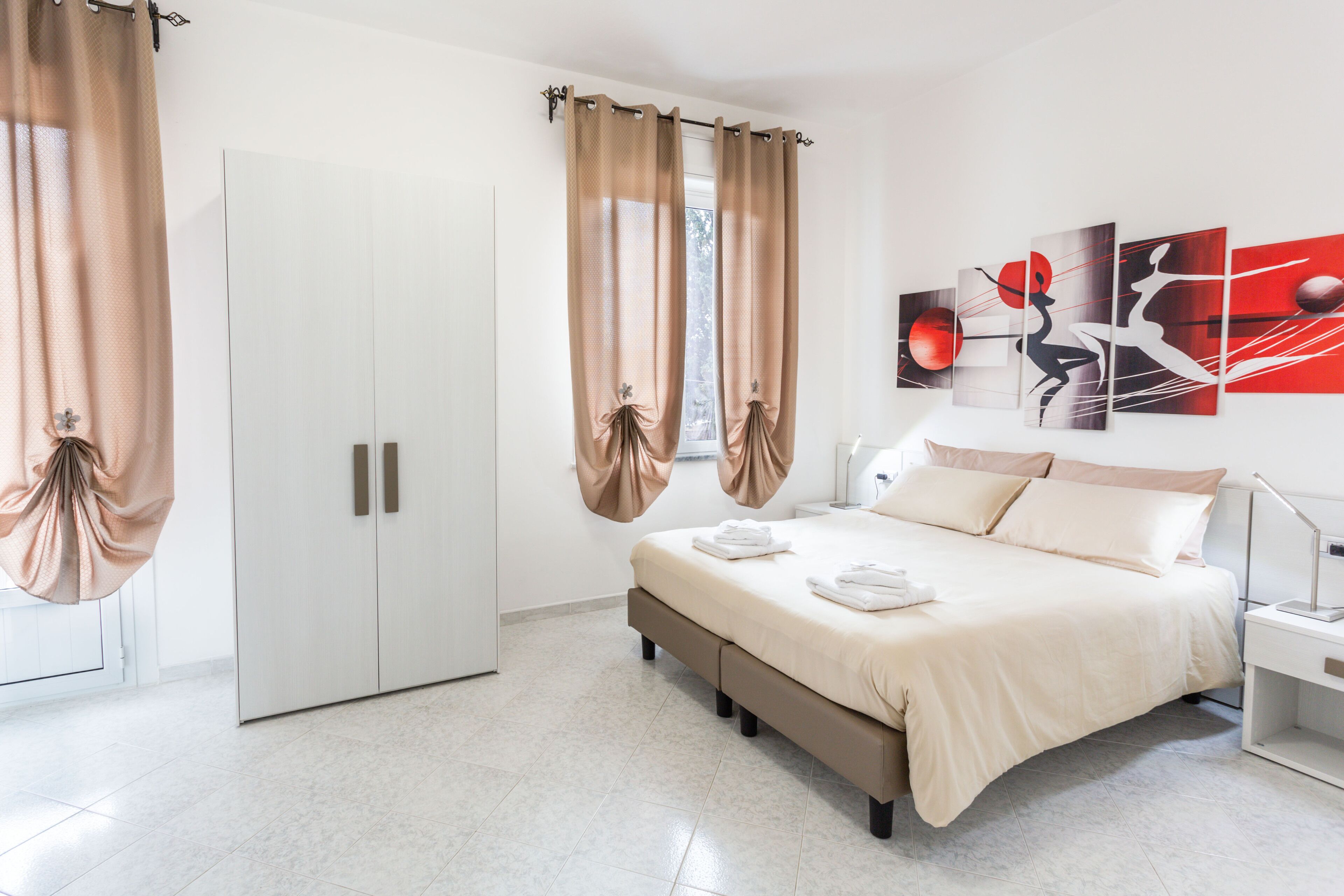 Quarto moderno com cama, cortinas, guarda-roupa e arte abstrata na parede.