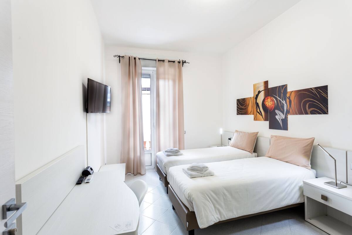 A hotel room with two beds, a TV, a desk, and a painting on the wall.