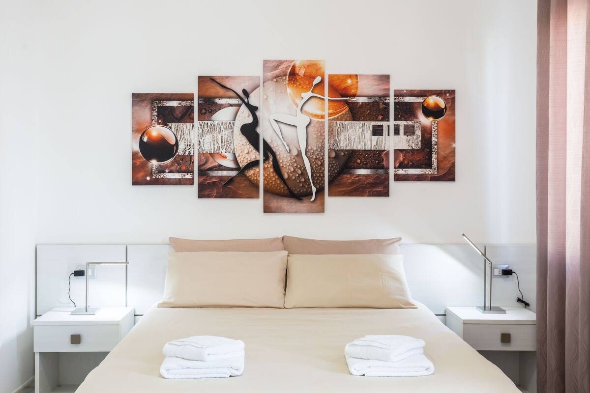 A hotel room with a large bed, two bedside tables, and a wall-mounted artwork.