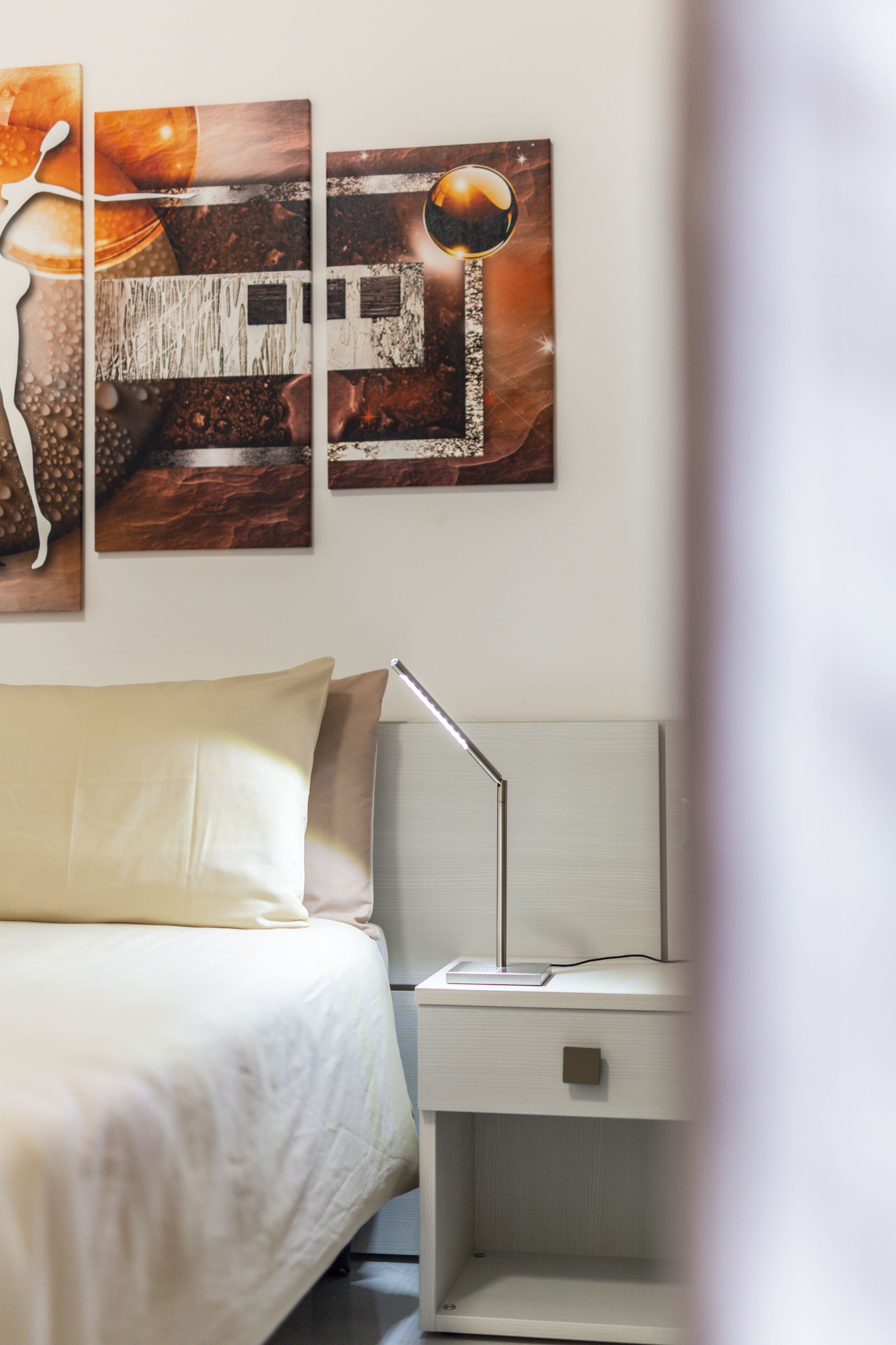 Een keurig opgemaakt slaapkamer met een bed, een nachtkastje en een aan de muur bevestigd kunstwerk.